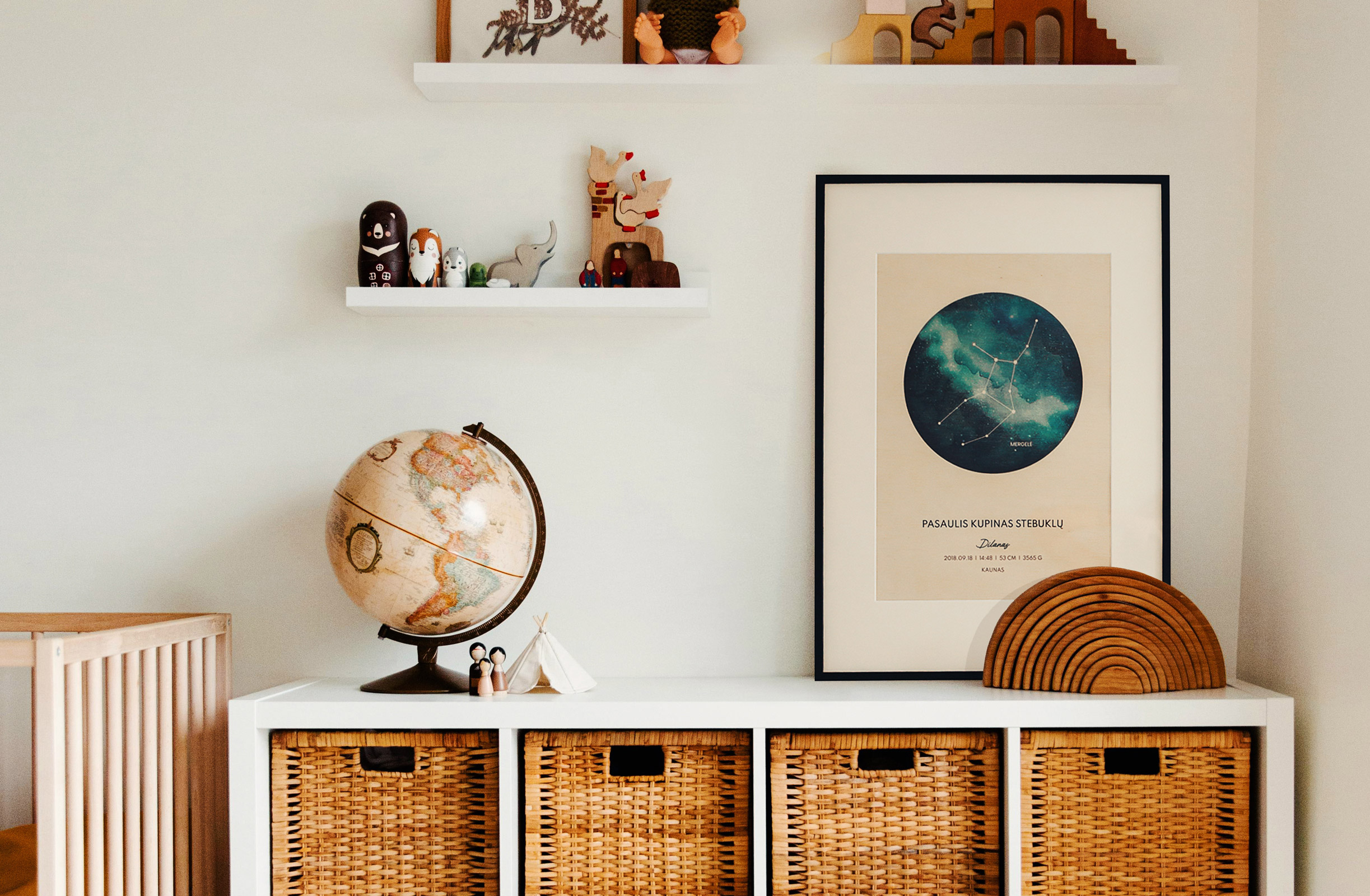 A cozy children's room corner with a white cabinet topped with a wicker basket, a globe, and animal figurines. Above the cabinet is a large framed print from a graphic design project for client Cozywood